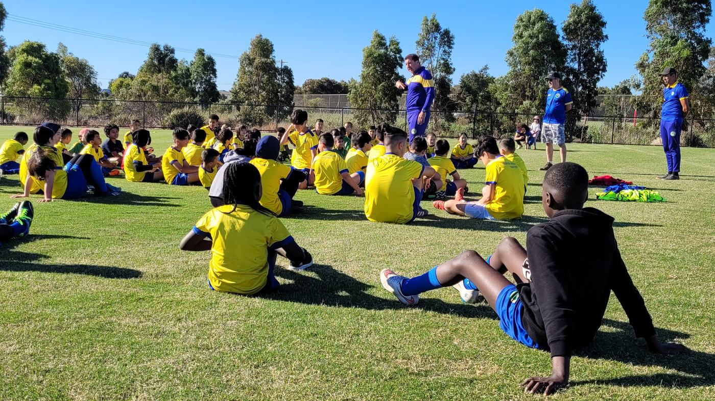 A coach addressing a group of young people at an outdoor soccer session